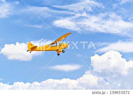 A yellow single-engine ultralight aircraft flying in a blue sky with white clouds. 139653872