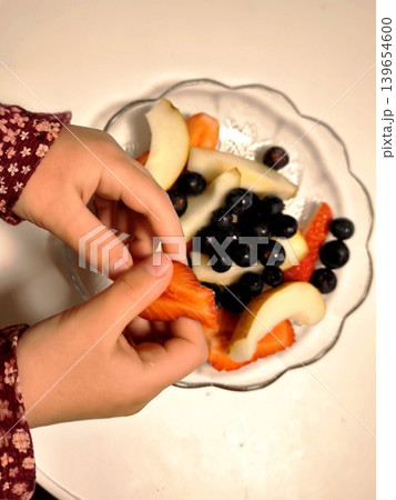A child picks fresh strawberries from a fruit bowl. A child picks fresh strawberries from a fruit bowl. 139654600