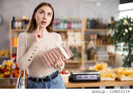 Girl looking at raw bbg sausage in store 139655214