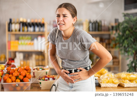 Young woman suffers from abdominal pain, feels pain in her stomach, while visiting grocery supermarket Young woman suffers from abdominal pain, feels pain in her stomach, while visiting grocery supermarket 139655248