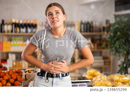Young woman with stomach pain in grocery store Young woman with stomach pain in grocery store 139655299