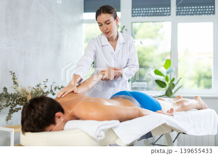 During massage, female physiotherapist stretche man client arm to improve mobility of shoulder joint 139655433