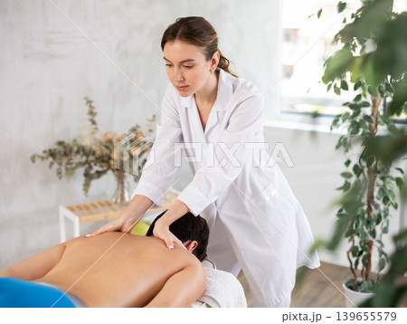 Professional young masseuse performing back massage for male patient 139655579