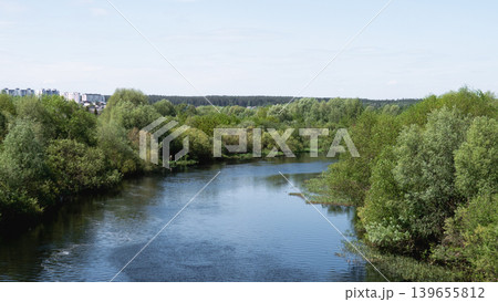 River Flowing Through Lush Green Trees Creating Tranquil Countryside Panorama With Gentle Ripples, Sunlit Sky, Mixed Deciduous Forest Along Meandering Bank, Distant Horizon And Clouds Reflecting River Flowing Through Lush Green Trees Creating Tranquil Countryside Panorama With Gentle Ripples, Sunlit Sky, Mixed Deciduous Forest Along Meandering Bank, Distant Horizon And Clouds Reflecting 139655812