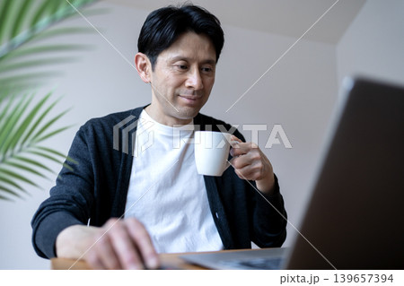 朝活でコーヒーを片手にパソコンを操作するミドル男性 139657394