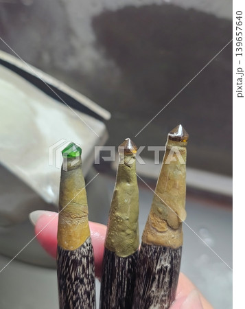 Small green and brown gemstones mounted on dop sticks for faceting and polishing in a workshop 139657640