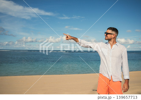 Man stands on sand, looking out at the water and pointing Man stands on sand, looking out at the water and pointing 139657713