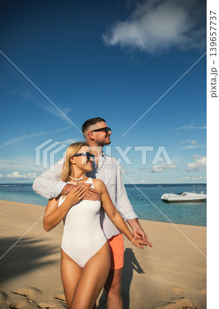 Couple stands together on sandy beach while looking at sea Couple stands together on sandy beach while looking at sea 139657737