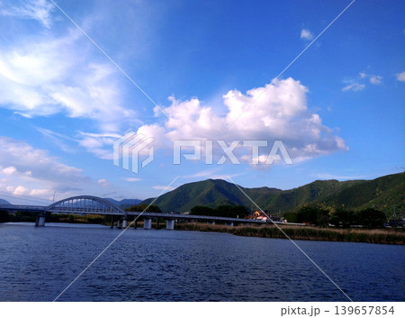 青空と雲が広がる川辺の橋と山並みの風景 139657854