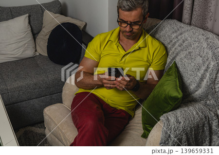 Man using smartphone while sitting in living room at home during evening Man using smartphone while sitting in living room at home during evening 139659331