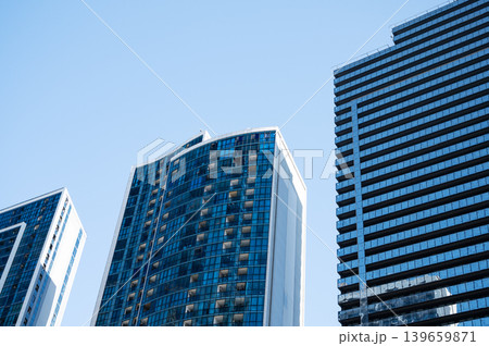 Modern high-rise residential buildings with glass facades against a clear blue sky. Modern high-rise residential buildings with glass facades against a clear blue sky. 139659871