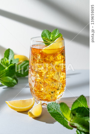 Iced tea with lemon and mint in a glass on a light background with shadows Iced tea with lemon and mint in a glass on a light background with shadows 139659895