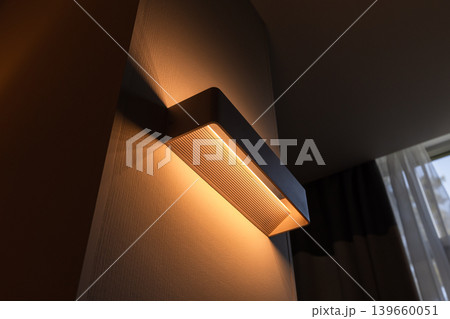 A modern wall sconce emits warm ambient light across a textured wall A modern wall sconce emits warm ambient light across a textured wall 139660051
