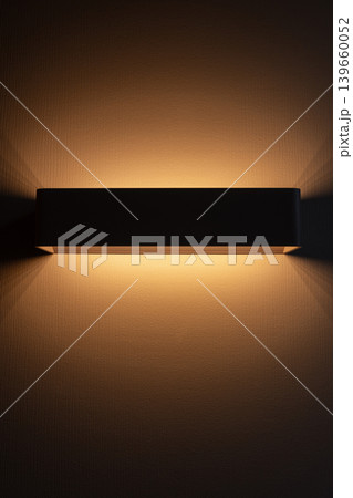 Warm wall sconce casts soft amber light across a textured wall Warm wall sconce casts soft amber light across a textured wall 139660052