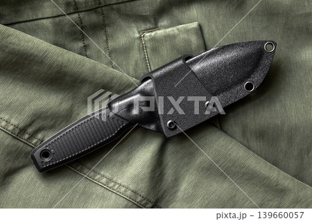 Tactical survival knife in a black kydex sheath rests on olive green military fabric 139660057