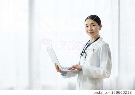 明るい窓辺でノートパソコンを操作する白衣を着た日本人女性医師 明るい窓辺でノートパソコンを操作する白衣を着た日本人女性医師 139660218