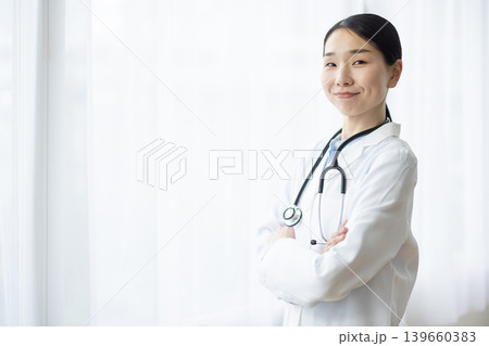 明るい窓辺で腕組みをして微笑む白衣を着た日本人女性医師 明るい窓辺で腕組みをして微笑む白衣を着た日本人女性医師 139660383