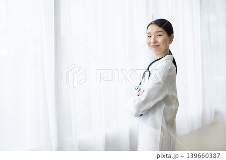 明るい窓辺で腕組みをして微笑む白衣を着た日本人女性医師 明るい窓辺で腕組みをして微笑む白衣を着た日本人女性医師 139660387