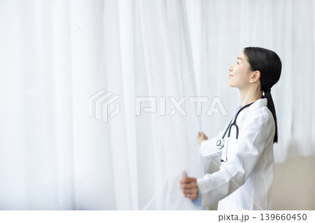 カーテンを開ける白衣を着た日本人女性医師 139660450