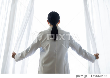 カーテンを開ける白衣を着た日本人女性医師 139660456