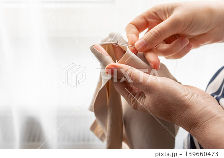 Woman darning a beige clothes by hand with needle and patch fabric Woman darning a beige clothes by hand with needle and patch fabric 139660473