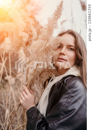 Woman reeds autumn portrait of a young lady holding dry pampas grass in a sunlit field during golden hour 139661359