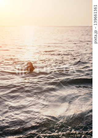 Woman swimming sunset young woman swims in the calm ocean water during a golden hour sunset with shimmering reflections Woman swimming sunset young woman swims in the calm ocean water during a golden hour sunset with shimmering reflections 139661361