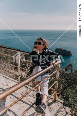 Woman coast travel stylish tourist in leather jacket leans on scenic railing overlooking deep blue sea on a sunny day 139661370