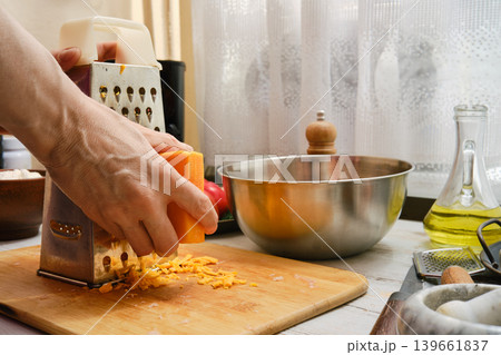 Hand grating orange cheese in a kitchen while preparing a meal during the day 139661837