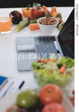 Young nutritionist showing bell peppers during an online video call consulting about healthy eating, sitting at home at a table with vegetables, laptop and measuring tape Young nutritionist showing bell peppers during an online video call consulting about healthy eating, sitting at home at a table with vegetables, laptop and measuring tape 139662332