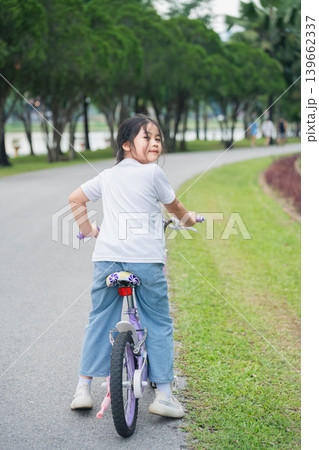 Young girl riding bicycle in park with green grass and trees, enjoying outdoor activity, leisure time, and joyful moment on a sunny day Young girl riding bicycle in park with green grass and trees, enjoying outdoor activity, leisure time, and joyful moment on a sunny day 139662337
