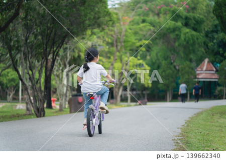 Child Riding Bicycle in Serene Park Setting Surrounded by Lush Green Trees and Pathway Ideal for Family Outdoor Activities and Leisure Time Child Riding Bicycle in Serene Park Setting Surrounded by Lush Green Trees and Pathway Ideal for Family Outdoor Activities and Leisure Time 139662340