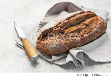 Rustic dark bread loaf with knife on napkin Rustic dark bread loaf with knife on napkin 139662908
