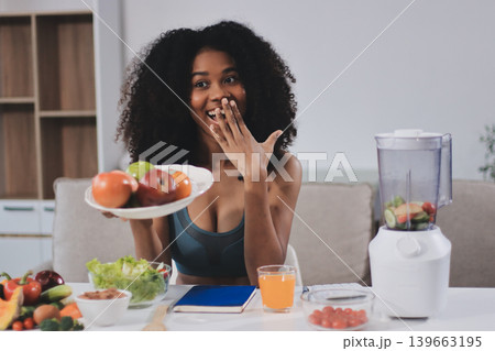 Young nutritionist showing bell peppers during an online video call consulting about healthy eating, sitting at home at a table with vegetables, laptop and measuring tape Young nutritionist showing bell peppers during an online video call consulting about healthy eating, sitting at home at a table with vegetables, laptop and measuring tape 139663195