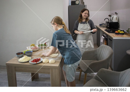 Happy mother and daughter cooking italian pizza together in cozy home kitchen. Happy mother and daughter cooking italian pizza together in cozy home kitchen. 139663662