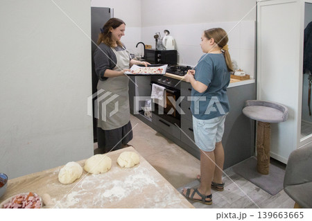 Pretty daughter and mother cooking italian pizza together in cozy domestic kitchen Pretty daughter and mother cooking italian pizza together in cozy domestic kitchen 139663665