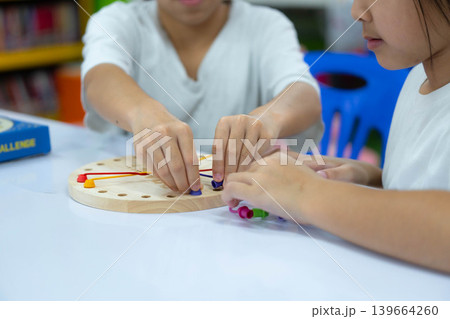 Two Asian little girls playing with wooden educational toy, developing fine motor skills and concentration in a classroom or home setting. Two Asian little girls playing with wooden educational toy, developing fine motor skills and concentration in a classroom or home setting. 139664260