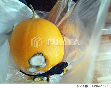 Bright orange pumpkin sits inside a transparent plastic bag, showing a large, circular patch of white and grey mold on its side. This image captures the natural process of food decay and spoilage Bright orange pumpkin sits inside a transparent plastic bag, showing a large, circular patch of white and grey mold on its side. This image captures the natural process of food decay and spoilage 139664377