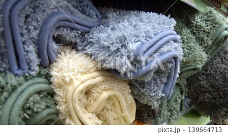 Soft, shaggy bath mats in various colors like blue, cream, and green are neatly folded on a store shelf. The thick, plush texture of the microfiber fabric is visible in this close-up retail shot 139664713