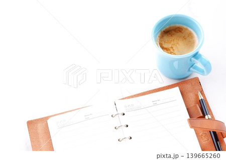 ミルクを入れたコーヒー、カフェ・ラッテを飲みながら、茶色の革のシステム手帳でデスクワーク中のイメージ ミルクを入れたコーヒー、カフェ・ラッテを飲みながら、茶色の革のシステム手帳でデスクワーク中のイメージ 139665260