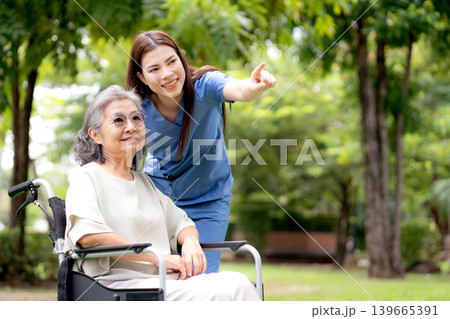 Caucasian female caregiver encouraging senior patient on wheelchair in garden. Caucasian female caregiver encouraging senior patient on wheelchair in garden. 139665391