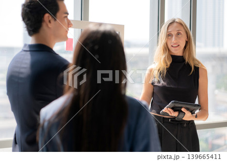 Caucasian businesswoman holding tablet presenting financial report on glass board. Caucasian businesswoman holding tablet presenting financial report on glass board. 139665411