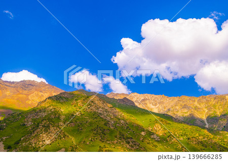 Mountain range with rocky peaks and green slopes under blue sky 139666285