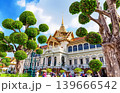 Colorful view of the Grand Palace in Bangkok, Thailand, featuring ornate Thai architecture, golden details, and manicured trees under a bright blue sky. 139666542