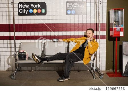 Laidback individual wearing yellow shirt enjoys downtime on city bench Laidback individual wearing yellow shirt enjoys downtime on city bench 139667258