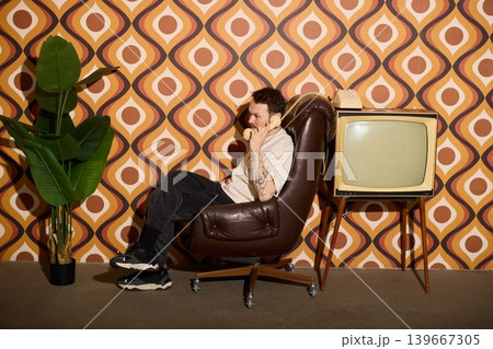 Individual sitting with retro television and patterned wall decor Individual sitting with retro television and patterned wall decor 139667305