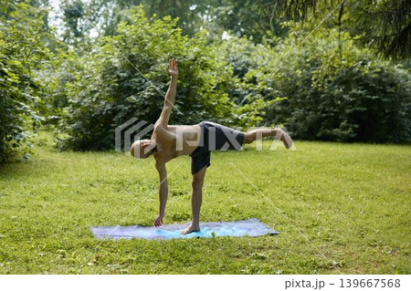 Individual performing extended leg pose with trainer on grass 139667568