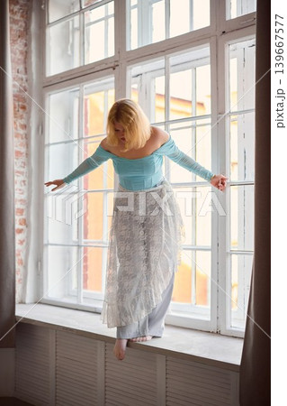 Interior setting featuring woman in fashionable clothing beside window Interior setting featuring woman in fashionable clothing beside window 139667577