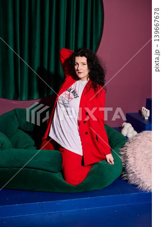 Woman in red suit seated on lush green setting with lively pose Woman in red suit seated on lush green setting with lively pose 139667678