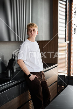 Individual casually supports himself on kitchen surface with steady gaze Individual casually supports himself on kitchen surface with steady gaze 139667695